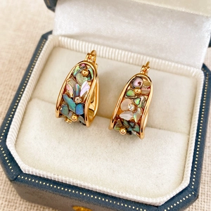 Macro shot of gold-plated U-shaped earrings featuring iridescent shell inlay and crystal detail