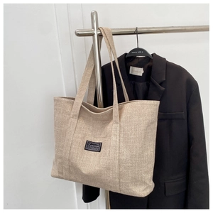 Close-up of beige canvas tote bag with fashion label hanging on a rack with a blazer