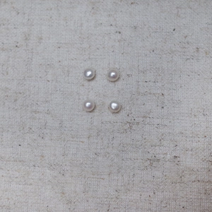 Macro shot of four polished white and pink flat round pearls on a linen fabric background