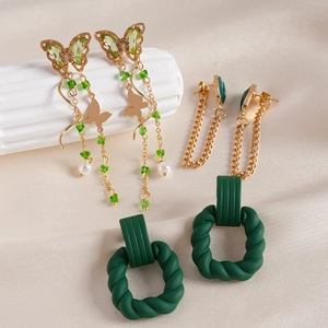 Detail of butterfly pearl drops, golden chain tassels, and green matte hoop earrings set