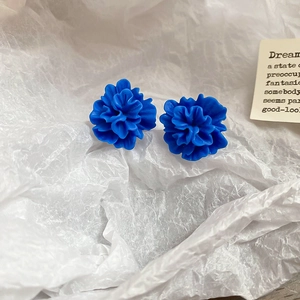 Macro shot of bright Klein blue resin flower stud earrings on white textured paper