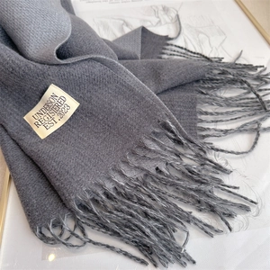 Detail view of grey soft cashmere-like scarf with fringe trim and brand tag on art background