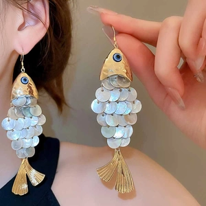 Detail of fish-shaped earrings with shell texture and golden metal tassels on model