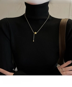 Detailed view of a gold Y-shaped ball pendant necklace worn over a black sweater