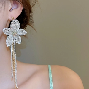 Detail of white crochet flower earring with long pearl and gold chain tassels