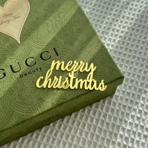 Close-up of golden acrylic Merry Christmas cake topper on an elegant gift box