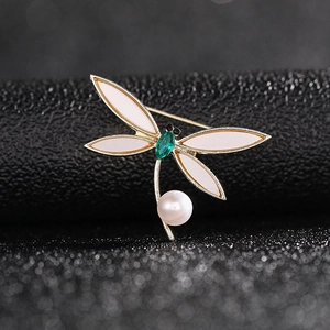 Macro shot of elegant dragonfly brooch with green gemstone, white enamel, and pearl detail