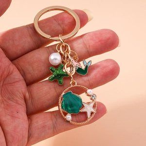 Golden keychain with mermaid, green starfish, shell and pearls on a soft background