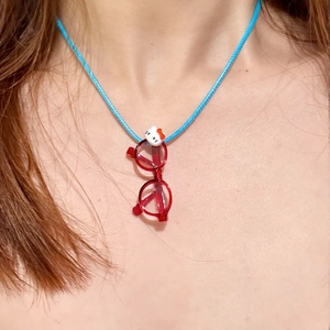 Detail of Hello Kitty red glasses pendant with bright blue braided cord necklace on model