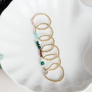 Detailed view of seven handmade golden beaded rings with colorful natural stones on ceramic