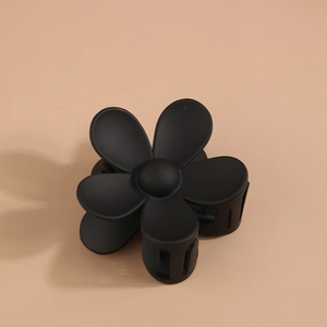 Détail d'une pince à cheveux en forme de fleur noire mate sur fond neutre