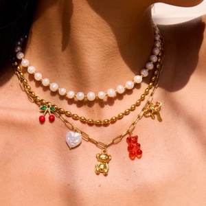 Layered gold necklaces with white pearls, red cherry and bear pendants on model