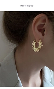 Close-up of elegant gold fan-shaped sunburst earrings worn by a model in a natural light