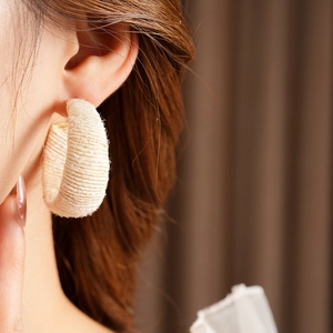 Close-up of a model wearing cream fabric woven C-shaped hoop earrings with a knit texture