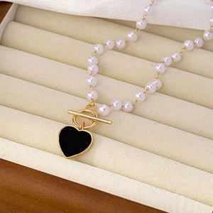 Elegant pearl necklace with black heart pendant and gold OT toggle clasp on beige jewelry box