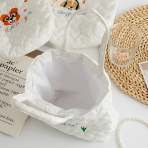 Close-up of white quilted tote bag featuring colorful dog embroidery and inner pocket