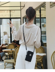 Détail du mini sac téléphone noir en nylon avec bandoulière réglable dans un café