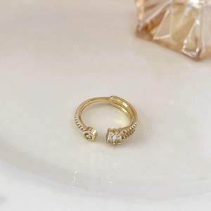 Dettaglio macro di anello aperto dorato con zirconi a taglio rotondo e baguette