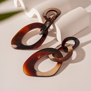 Exaggerated geometric resin earrings with amber tortoiseshell pattern on white stand