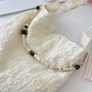 Detail of cream lace shoulder bag featuring floral embroidery and acrylic beaded chain