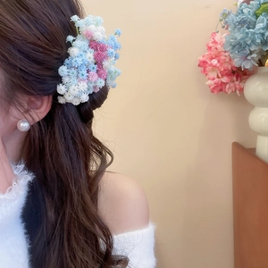 Detail of floral hair clip with white, blue, and pink petals worn on a model hair