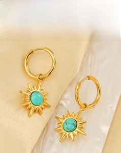 Detail of vintage gold sun earrings with turquoise center on marble and silk