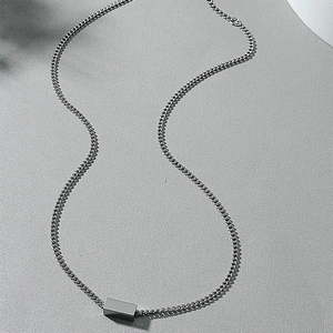 Macro shot of silver cube pendant on curb chain with matte grey textured background