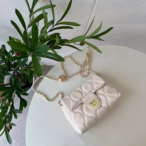Detail of beige quilted handbag with golden chain strap and rotary lock on a white table