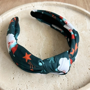 Top view of green fabric Christmas headband with Santa print and knotted detail on tray