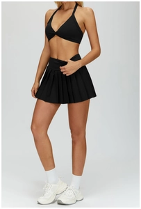 Detail of a black halter yoga bra and pleated tennis skirt set on a model