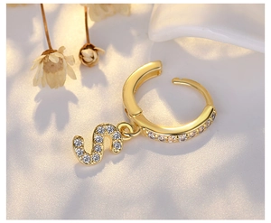 Macro detail of gold S-letter pendant earring with pavé zircon setting on white background