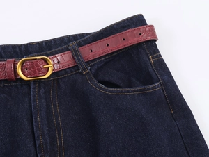 Détail du jean taille haute avec ceinture en cuir bordeaux embossé crocodile et boucle dorée