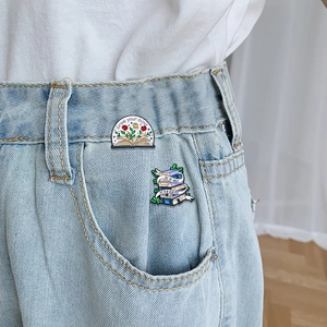 Cartoon enamel book pins featuring floral motifs and motivational quotes on denim fabric