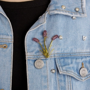 Close-up of lavender brooch with purple crystals pinned on light blue denim jacket