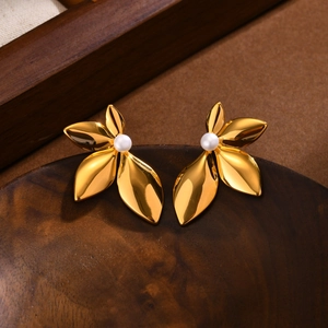 Élégantes boucles d'oreilles feuilles dorées avec perles sur un bol en bois vintage