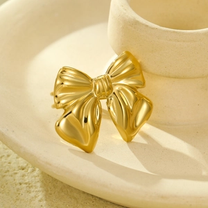 Polished 18K gold bow-shaped stainless steel ring on a minimalist ceramic plate