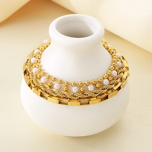 Close-up of stacked 18K gold plated chain bracelets with pearls on a white ceramic vase