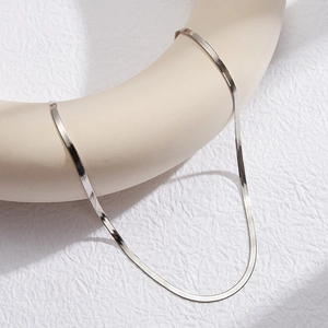 Detailed view of silver flat snake chain draped over a beige minimalist prop