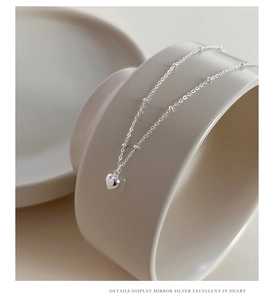 Close-up detail of silver heart pendant with delicate beaded chain on ceramic background