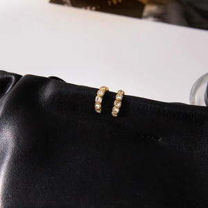 Close-up of gold semi-circle earrings with clear cubic zirconia on black leather