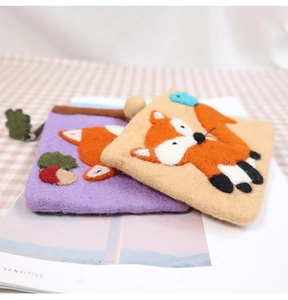 Close-up of wool felt pouches featuring fox and bird embroidery with leaf zipper pull