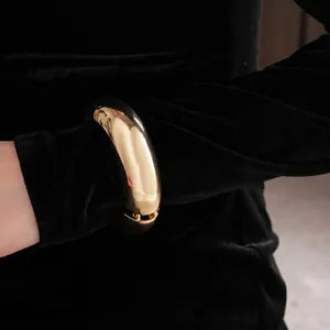 Minimalist wide gold metal bangle bracelet with polished mirror finish on a black sleeve