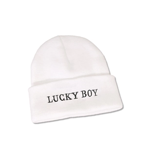 Close-up of white knitted beanie featuring black LUCKY BOY embroidery text detail