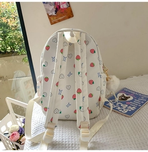 Close-up of white student backpack featuring strawberry patterns and a white pompom pendant