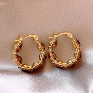 Detail macro shot of 18k gold plated round earrings with amber brown stones on silk fabric