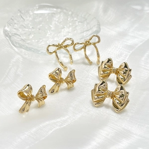 Close-up of three vintage gold bow stud earrings set on elegant white silk fabric