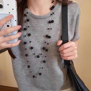 Detailed view of layered long sweater necklace with black beads on a grey knit top