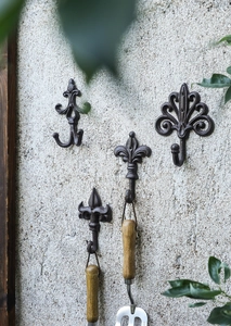 Close-up of vintage cast iron hooks holding rustic gardening tools on a concrete wall