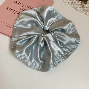 Close-up of light blue satin scrunchie showing elegant silk texture and fabric folds