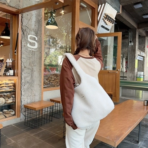 Close-up of white plush tote bag with soft texture and wide shoulder strap in a cafe